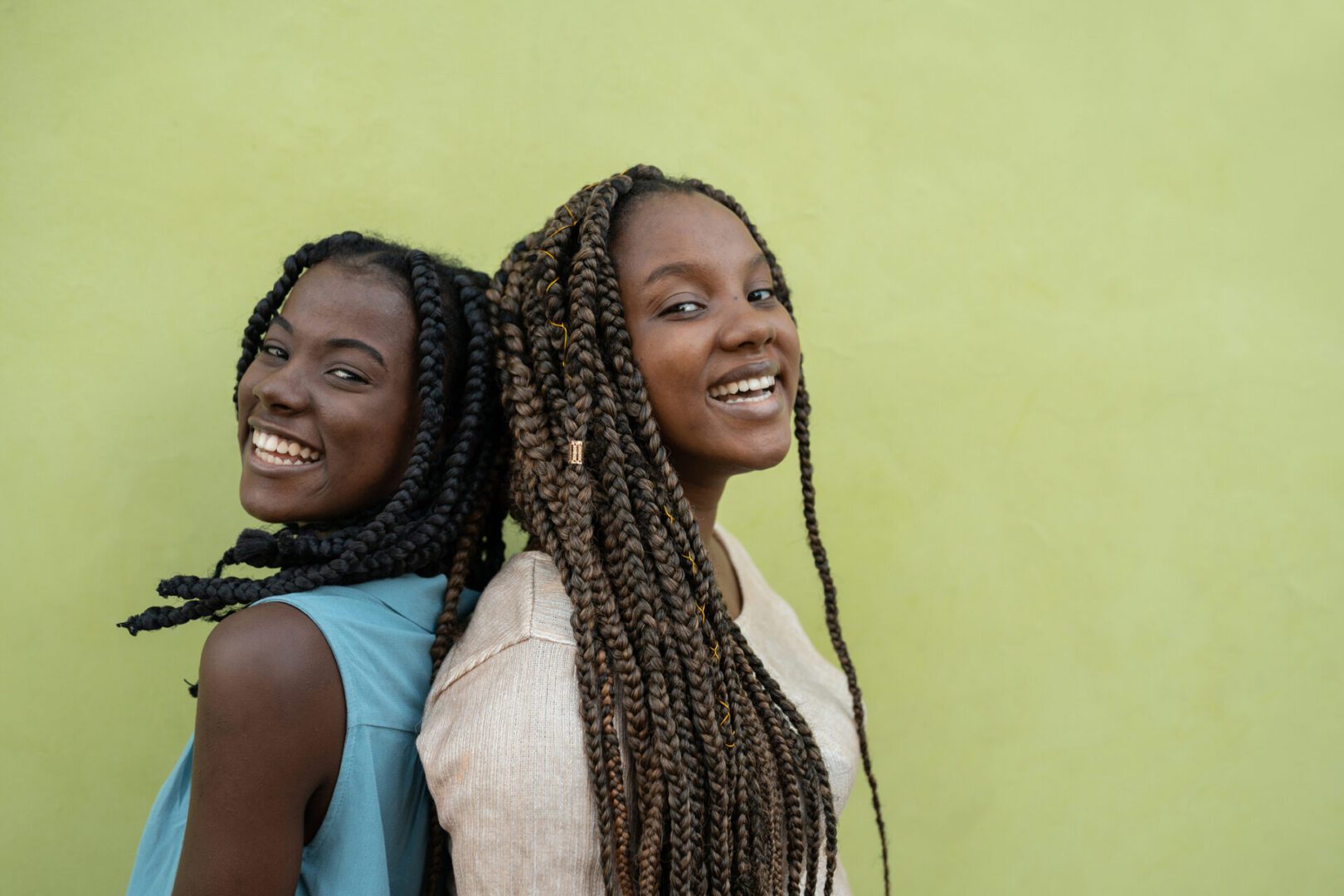 Two women smiling back-to-back against green background.